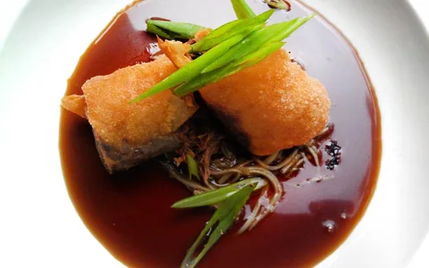 A golden appetizer served with greens and sauce.