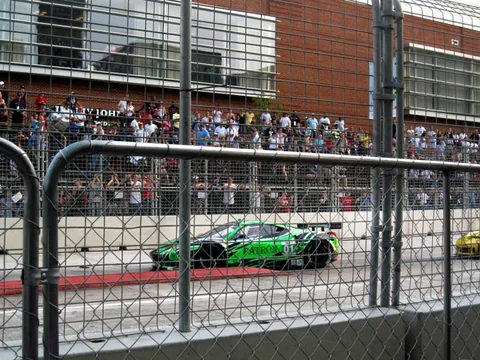 Green race car on the circuit beside a brick building.